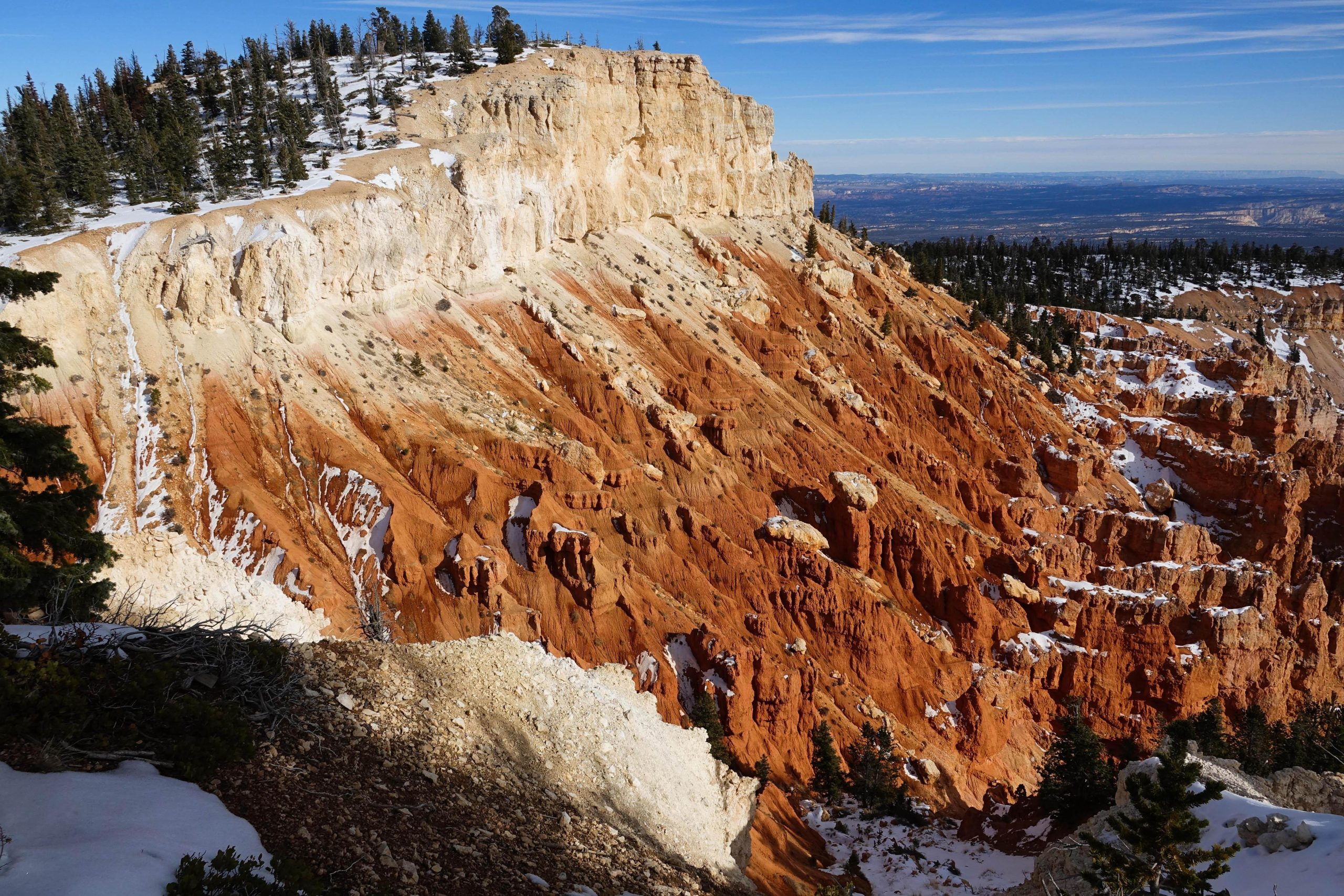View over Bryce Canyon Amphitheater's red hoodoo cliffs from the rim, with snow dusting the pinnacles and pine trees.