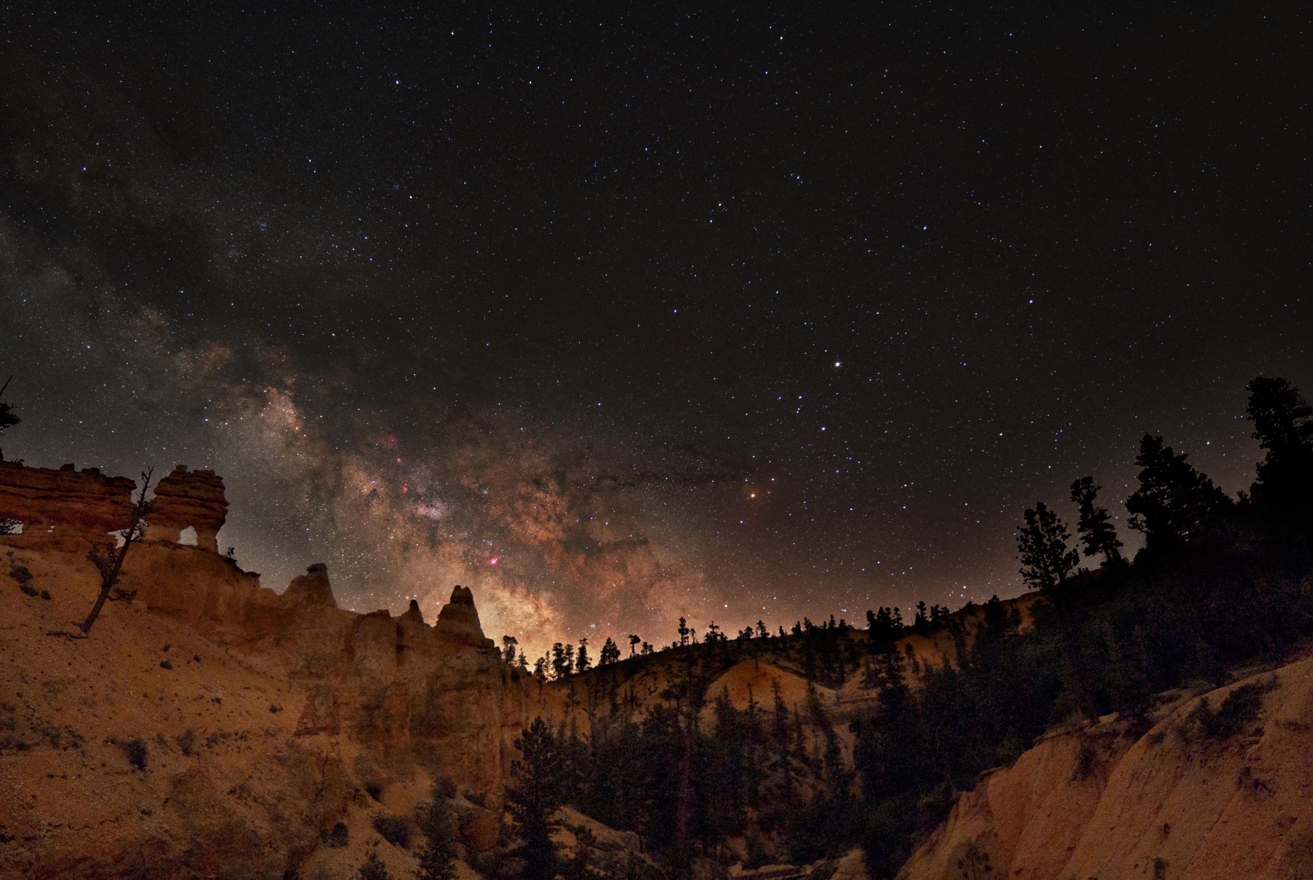 Milky Way arches over Bryce Canyon hoodoos in a star-filled night sky above the park.