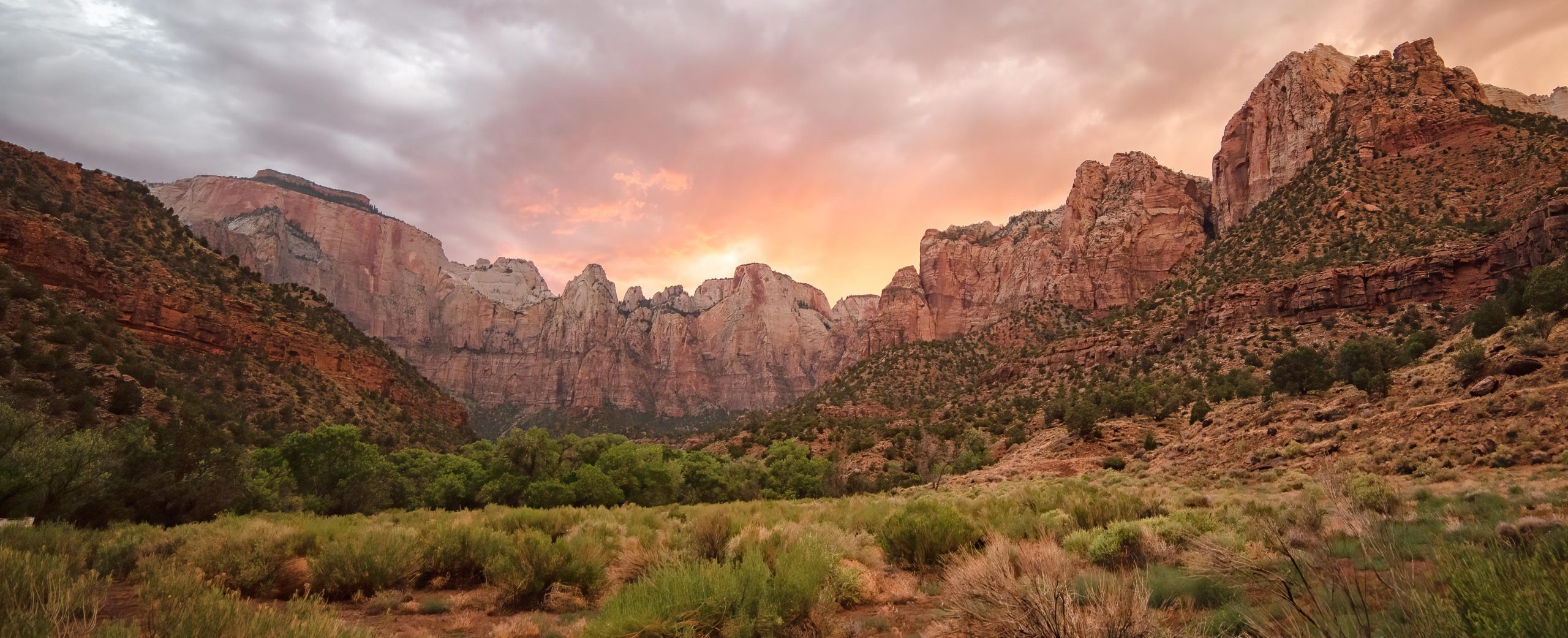 Zion Canyon view in Zion National Park at sunset with towering red rock cliffs and green valley below.