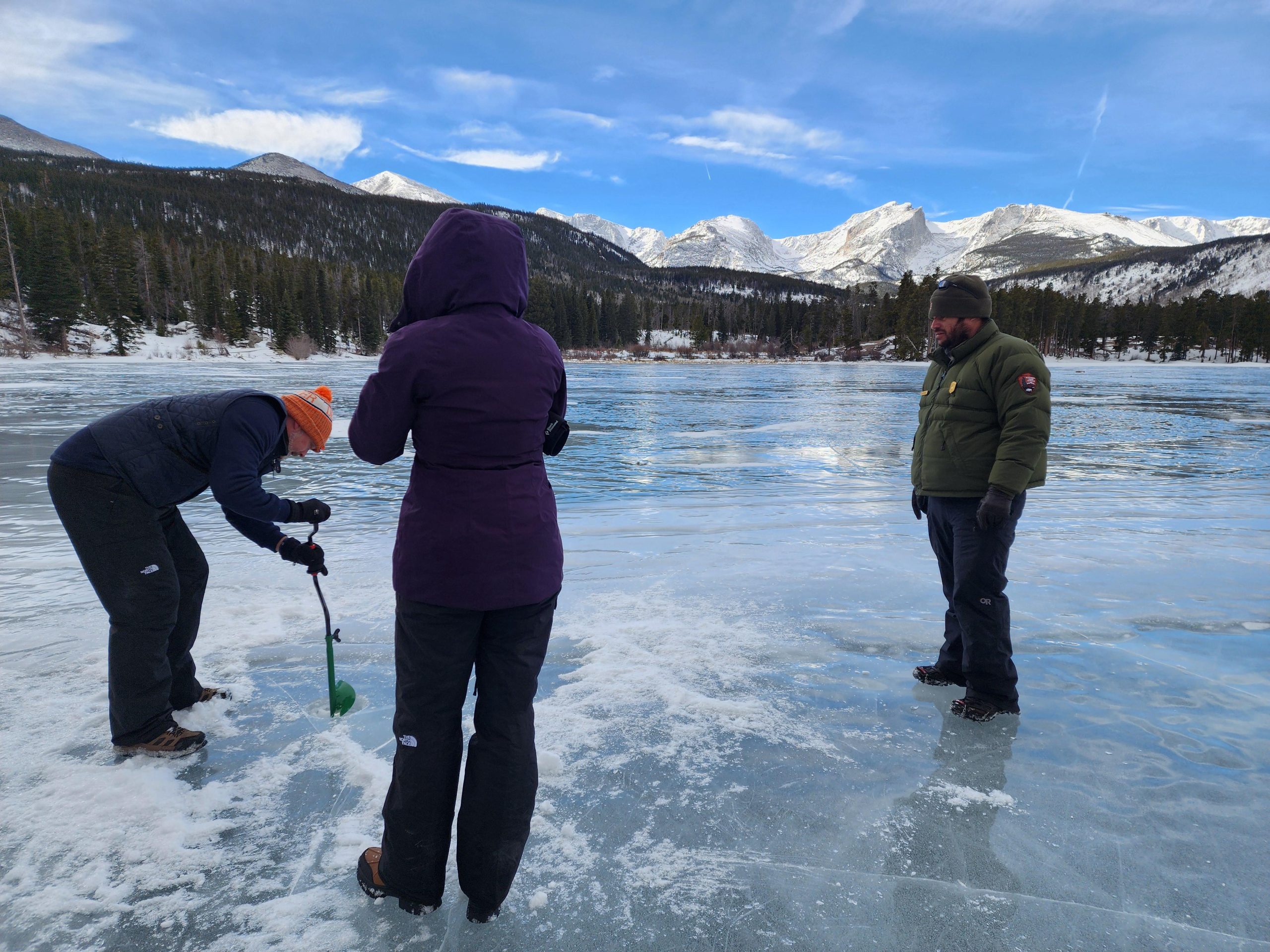 Figures drill into the frozen Bear Lake in Rocky Mountain National Park, snow-capped peaks in the background.