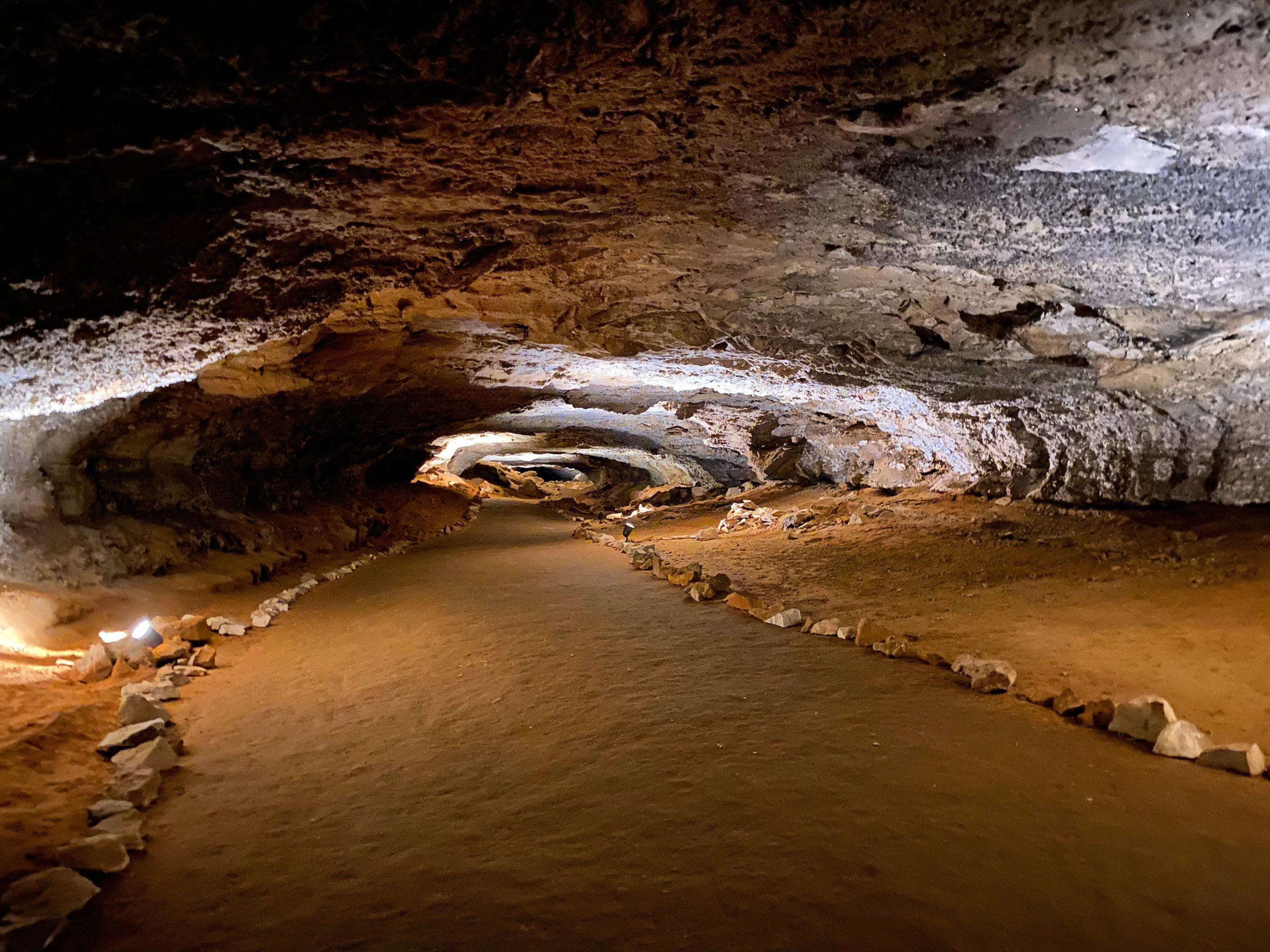Inside Mammoth Cave National Park, a dimly lit underground passage with a stone-lined path winding through rugged cavern walls.