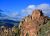 Pink and brown rock spires of Pinnacles National Park rise above pine trees under a bright blue sky.