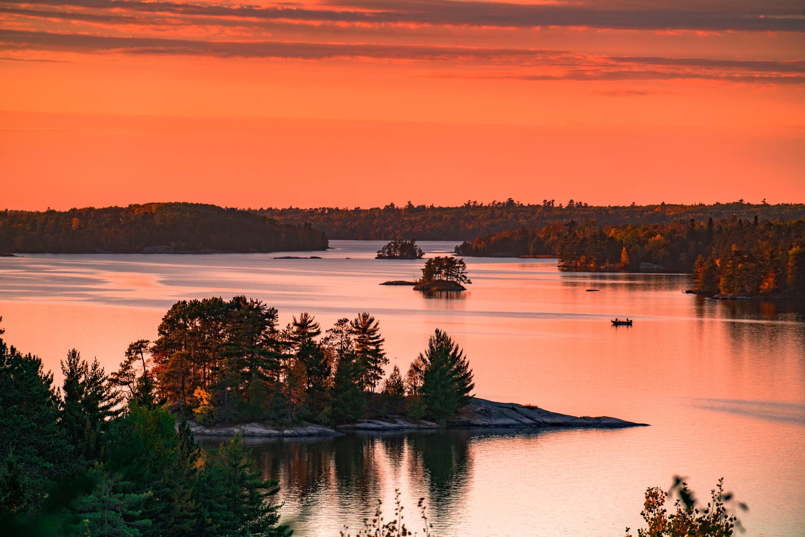 Sunset over the calm lakes and pine islands of Voyageurs National Park, with orange skies reflecting on tranquil water.