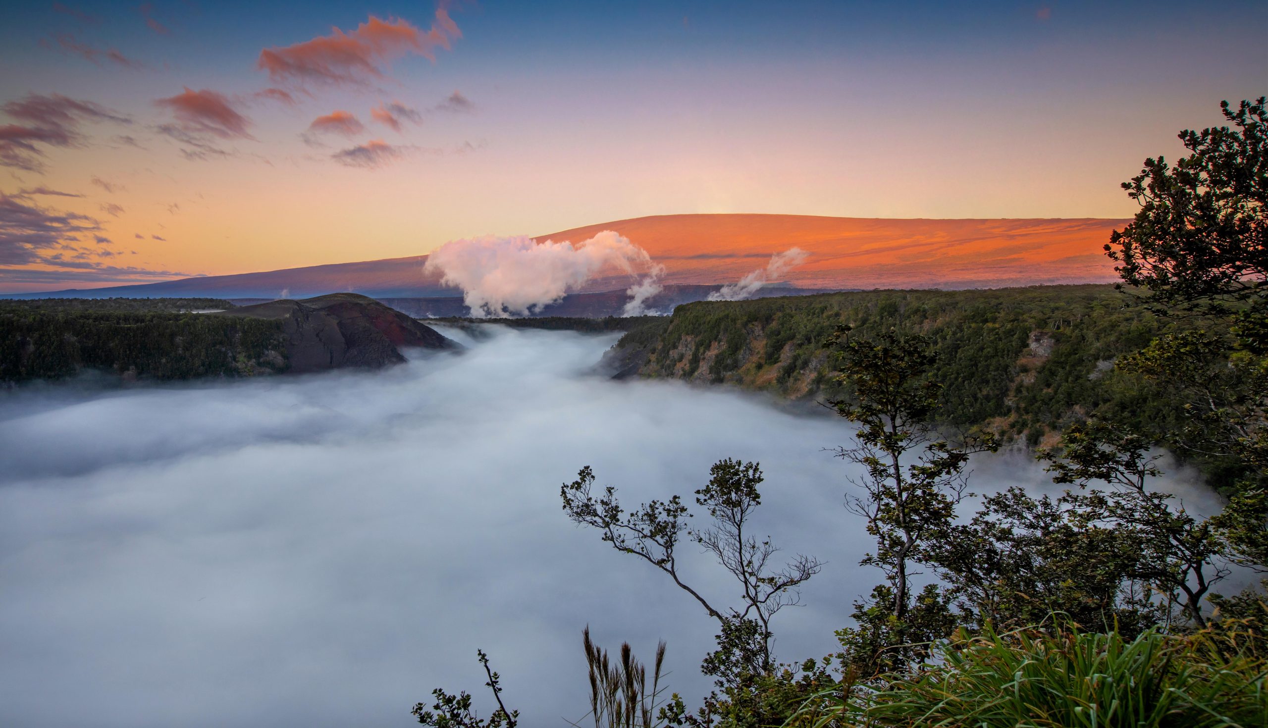 Sunrise over Halemaʻumaʻu Crater overlook in Hawaiʻi Volcanoes National Park, steam rising from the crater rim.