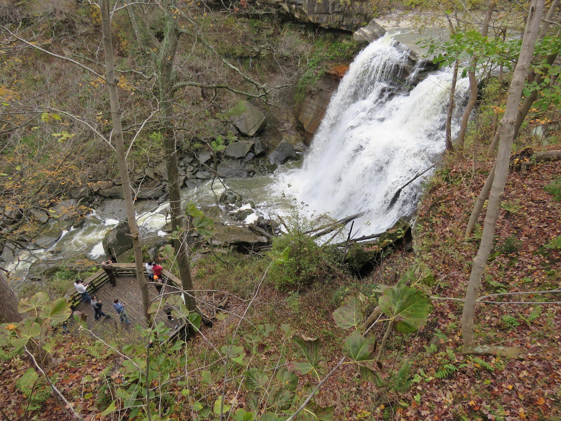 Brandywine Falls in Cuyahoga Valley National Park cascades over rock ledges beside a wooden overlook with visitors.