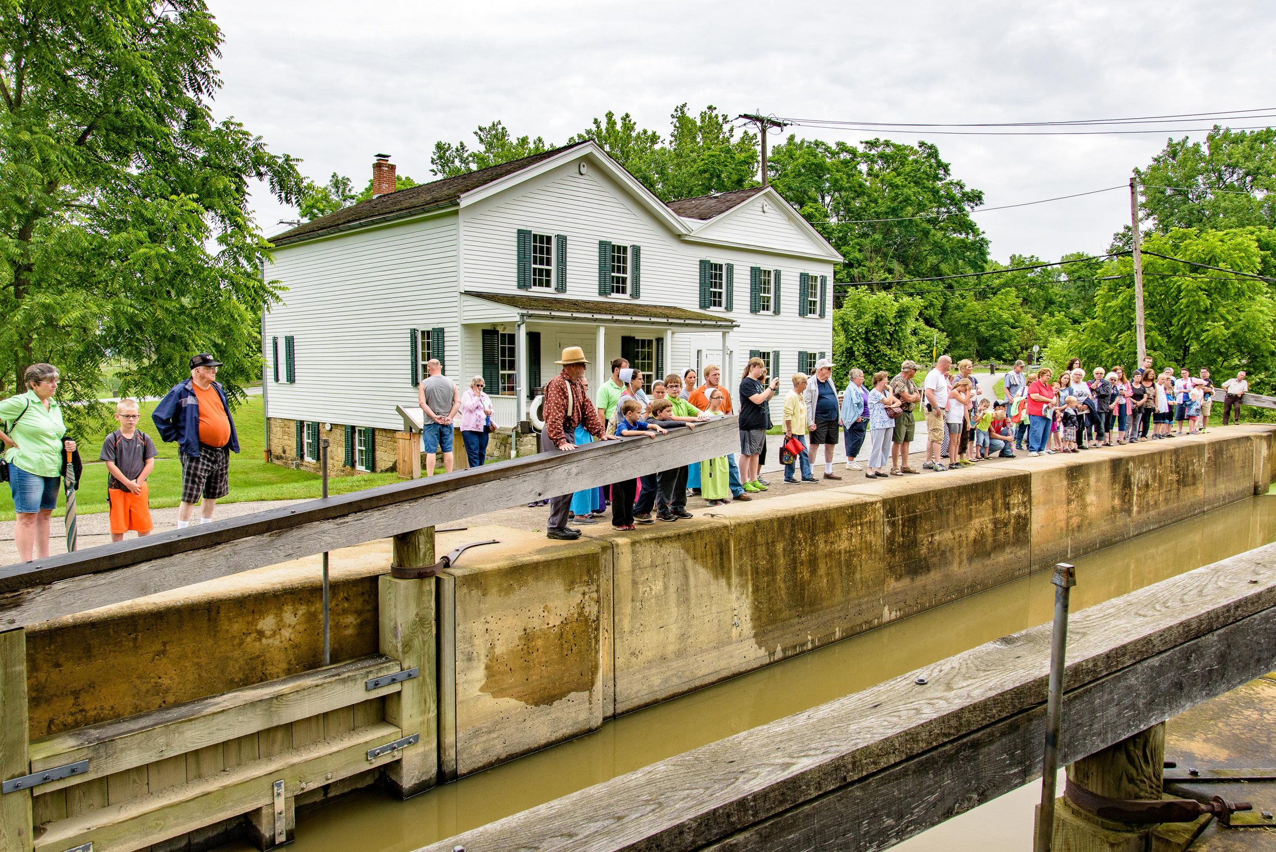 Crowd of visitors along the Ohio & Erie Canal lock near a white historic house in Cuyahoga Valley National Park.
