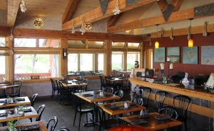 Rustic dining room inside a lodge-style restaurant at Capitol Reef National Park, featuring exposed timber beams and large windows.