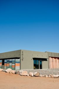 Exterior of a modern hotel along a desert landscape at Capitol Reef National Park, with colorful window panels and a gravel foreground.