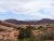 Red sandstone mesas and desert shrubs spread across a wide canyon under a partly cloudy blue sky in Arches National Park.