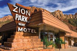 Lodging sign at a motel near the entrance to Zion National Park with towering red rock cliffs behind.