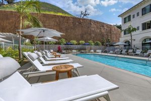 Sun-soaked pool deck with white loungers and umbrellas at a Malibu lodging property near Channel Islands National Park, offering ocean breeze and palm shade.