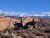 Red sandstone spires rise in Arches National Park, with snow-dusted plains and distant blue mountains under a clear sky.