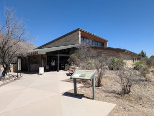 Visitor center at Carlsbad Caverns National Park sits along a sunlit plaza with desert shrubs and a stone building.