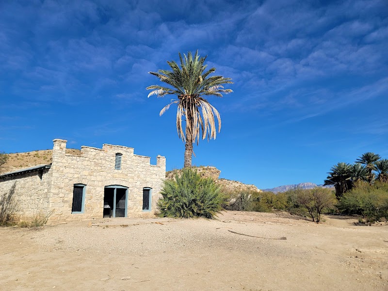 Hot Springs Trailhead at Big Bend National Park with a stone building, palm trees, and desert surroundings.
