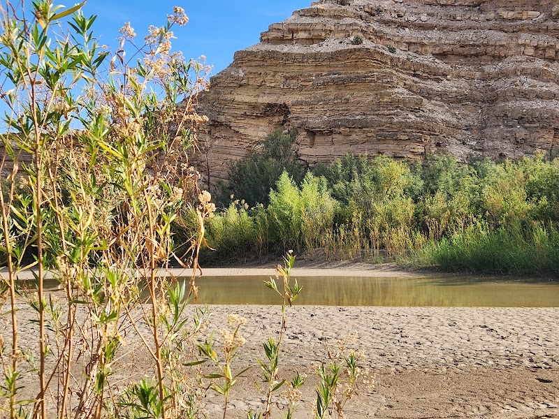 Hot Springs Trailhead at Big Bend National Park, showing a sandy riverbank, spring-fed water and rugged bluff.