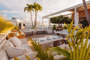 Rooftop lounge at 1 Hotel South Beach in Biscayne National Park, with palm trees, white seating, and dining setups under a sunny sky.