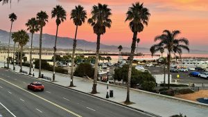 Palm-lined promenade and marina along a coastline at Ventura Harbor near Channel Islands coastline at sunset.