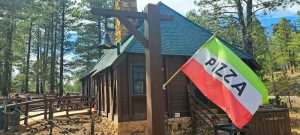 Pizza restaurant in Bryce Canyon National Park sits beside a rustic wooden building with a colorful flag.