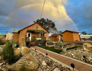 Wooden lodge cabins at Circle of Destination Motel complex in Capitol Reef National Park under a vibrant double rainbow.