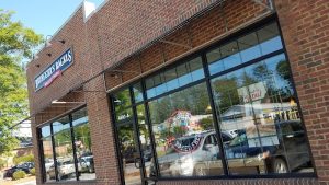 Bagel shop storefront in a brick building near Congaree National Park, with large glass windows reflecting a street scene.