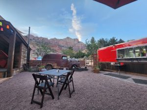 Outdoor seating at Bit & Spur Restaurant & Saloon in Zion National Park, with a vintage truck and red canyon walls in the background.
