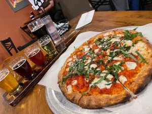 Pizza and beer flight at a park-side eatery near Carlsbad Caverns National Park, with a large pepperoni pizza on a wooden table.