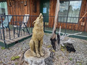 The Woodsman Country Lodge front porch near Crater Lake, featuring a carved wolf statue on a stump and rustic wood siding.