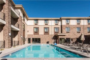 Moab hotel pool courtyard at Canyonlands National Park area, with a multi-story brick-and-stone lodging building and bright blue sky.