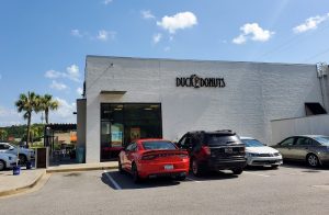 Exterior of a white brick storefront with large glass windows and several parked cars in front, near Congaree National Park.