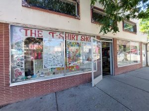 Storefront with large glass windows covered in colorful posters and stickers, an open door, brick facade near Arches National Park.