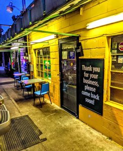 Exterior of Reggae Grill in Congaree National Park, a small roadside restaurant with yellow walls and blue chairs along a narrow outdoor seating area.