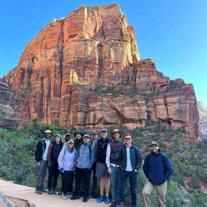 Group of hikers posing in front of a towering red sandstone cliff in Zion National Park.