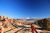 Sunlit red rock formations and a wooden railing overlook Fiery Furnace in Arches National Park, with distant snow-capped mountains.