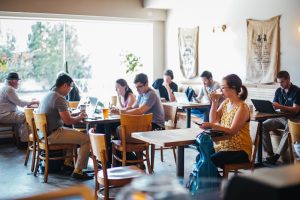 Interior of a bright cafe inside Congaree National Park where visitors work on laptops and chat at shared tables.