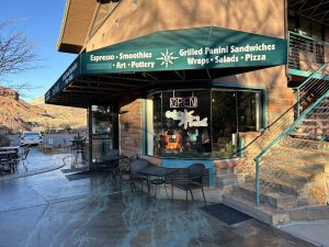 Cafe Soleil exterior with a teal-green awning and outdoor seating on a stone storefront in Zion National Park.
