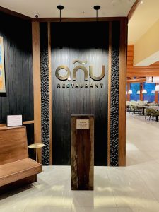 Interior of Añu Restaurant at Zion National Park with dark wood panels and a gold-toned sign above a pedestal.