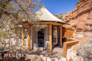 Lodging cabin with a canvas roof and wooden deck set against red rock cliffs in Zion National Park.