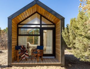 Ofland Escalante cabin lodging in Capitol Reef National Park sits on a sandy desert hillside with cedar trees and a covered porch.