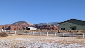 Exterior view of a lodge at Capitol Reef National Park near Torrey, with red rock cliffs behind a white fence.