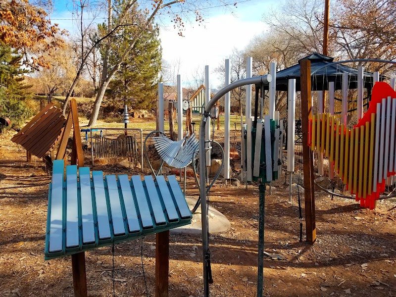 Colorful wind-chime sculptures and wooden structures at Rotary Park, Arches National Park, with autumn trees and sandy ground.
