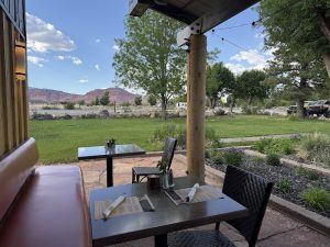 Outdoor restaurant patio at Capitol Reef National Park with green lawn and distant red rock cliffs under a bright blue sky.
