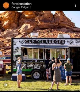 Capitol Reef National Park food truck serving burgers sits beside red rock cliffs, offering a casual lunch stop.