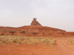 Red desert landscape in Arches National Park, featuring a layered rock formation with a flat cap rock and a dirt road.