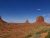 Desert panorama in Arches National Park with two large red sandstone buttes, sparse vegetation, and a clear blue sky.