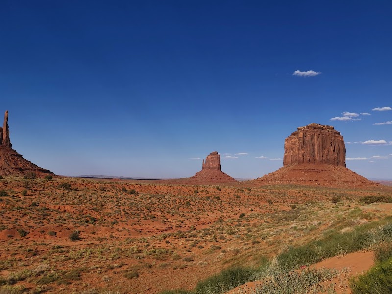 Desert panorama in Arches National Park with two large red sandstone buttes, sparse vegetation, and a clear blue sky.