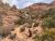 Arches National Park red rock canyon with a narrow waterfall down a sandstone ledge, desert shrubs, and a rocky dirt trail in the foreground.