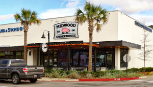 Restaurant exterior near Congaree National Park, with palm trees and outdoor seating along a sidewalk.