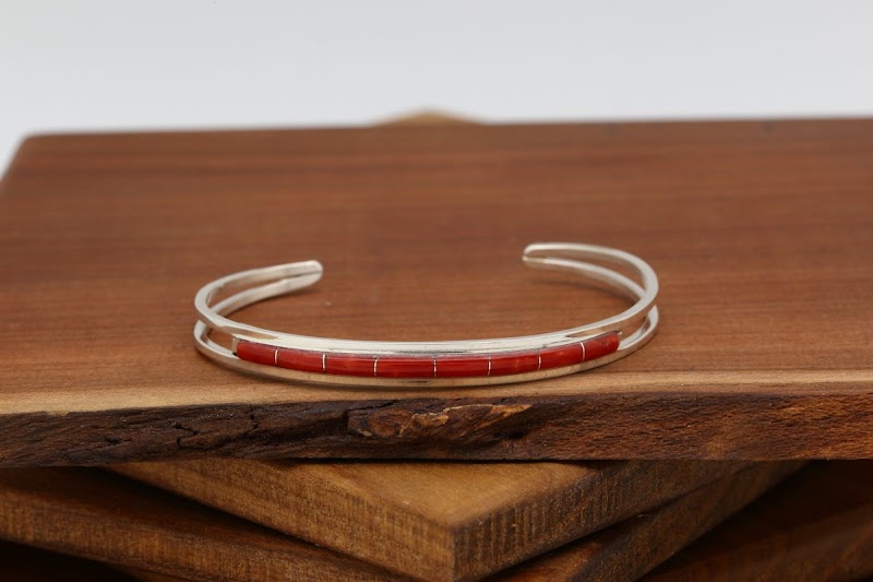 Silver cuff bracelet with red segmented inlay rests on stacked wooden boards at Arches National Park.
