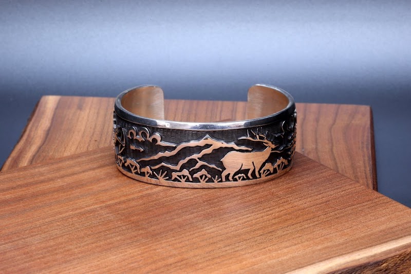 Copper cuff bracelet with a desert scene, including a deer and distant mountains, displayed on a wooden pedestal at Arches National Park.