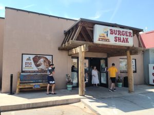 Burger Shak exterior at Capitol Reef National Park with wooden posts and a bright sign, people entering a small dining building.